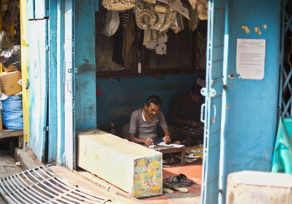 An artisan working inside a small shop with blue doors in Kolkata, India.