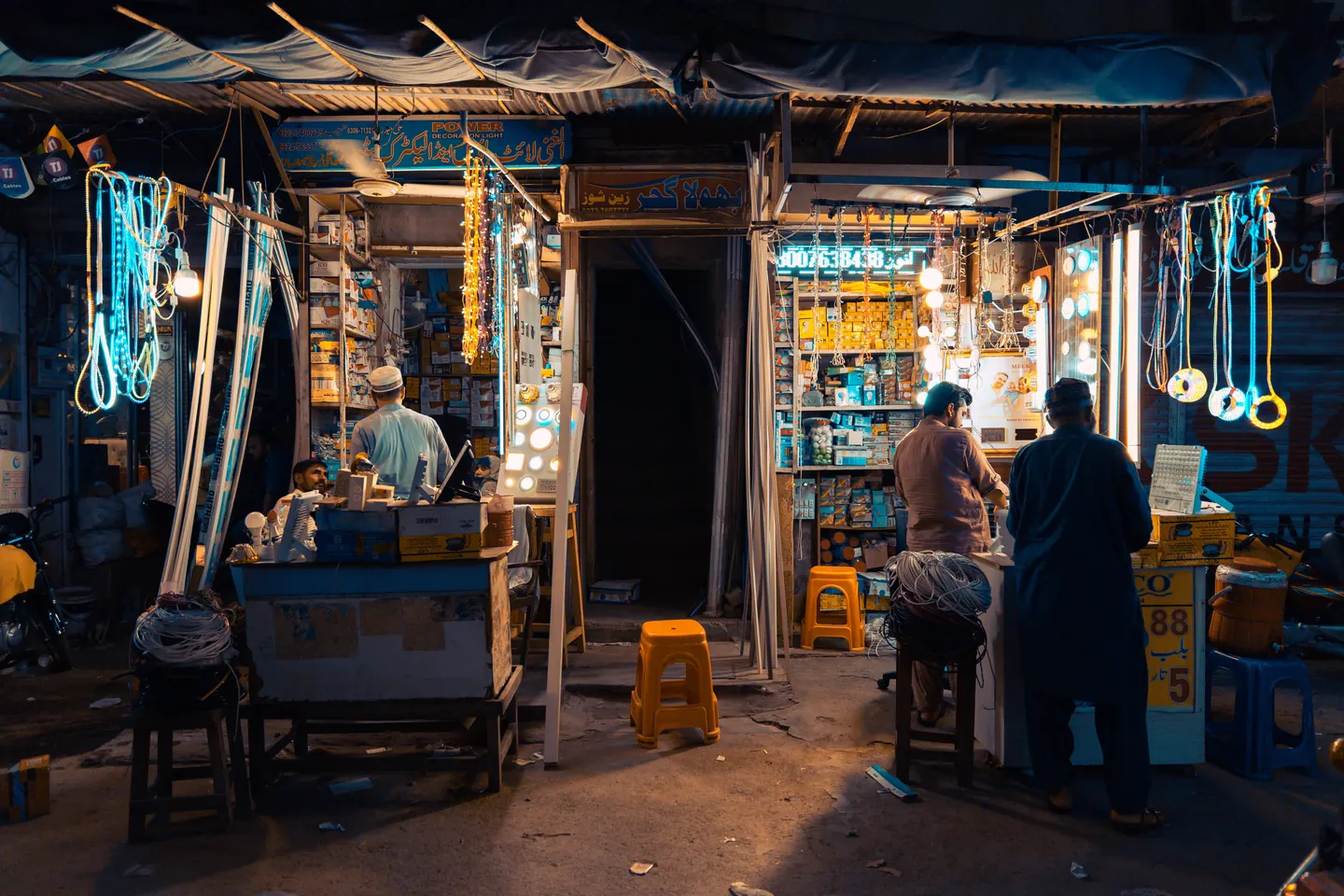 A brightly lit shop at night with customers at the counter and motorbikes parked outside.