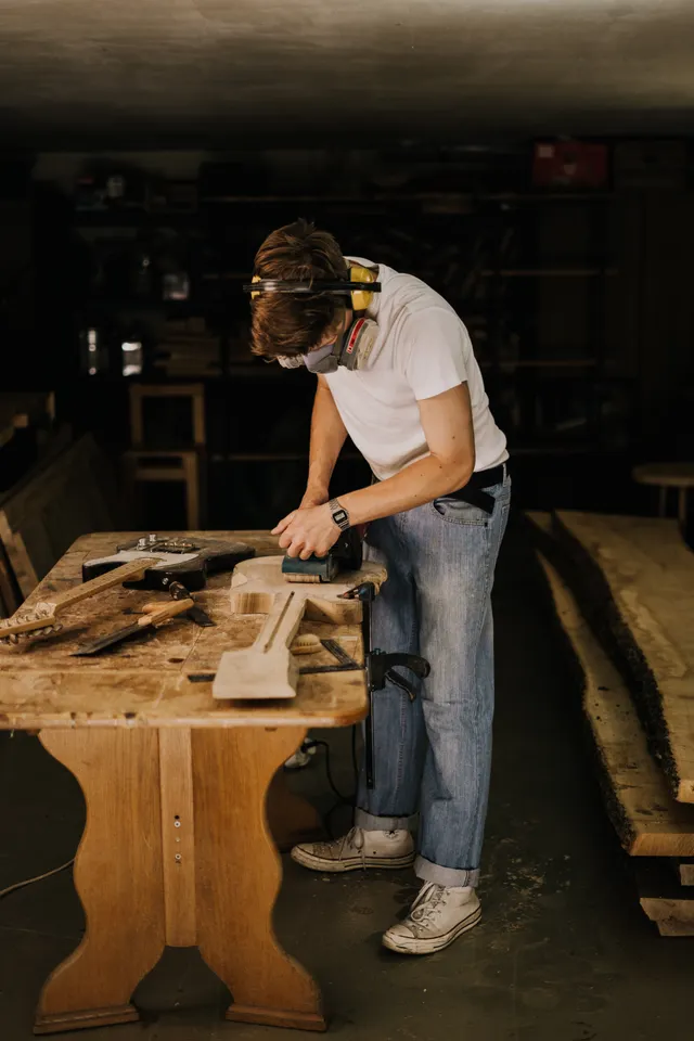 A woodworker carefully sanding a wooden instrument body in a workshop.